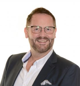 Head and shoulders shot of smiling Brian Cape in suit and glasses