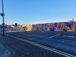 Colourful wall mural beneath blue sky in empty road, saying WEST BROMWICH