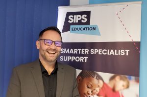 Smiling Brian Cape of SIPS Education standing in front of a pull-up banner which says 'Smarter specialist support'