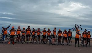 A line of cyclists wearing orange tops against a backdrop of grey clouds