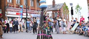 People in a town centre around a woman in costume with a pot balanced on her head