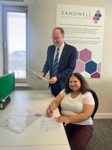 Alan Taylor and Anjali Agrawal signing the Sandwell Business Ambassadors' charter, with an SBA poster in the background