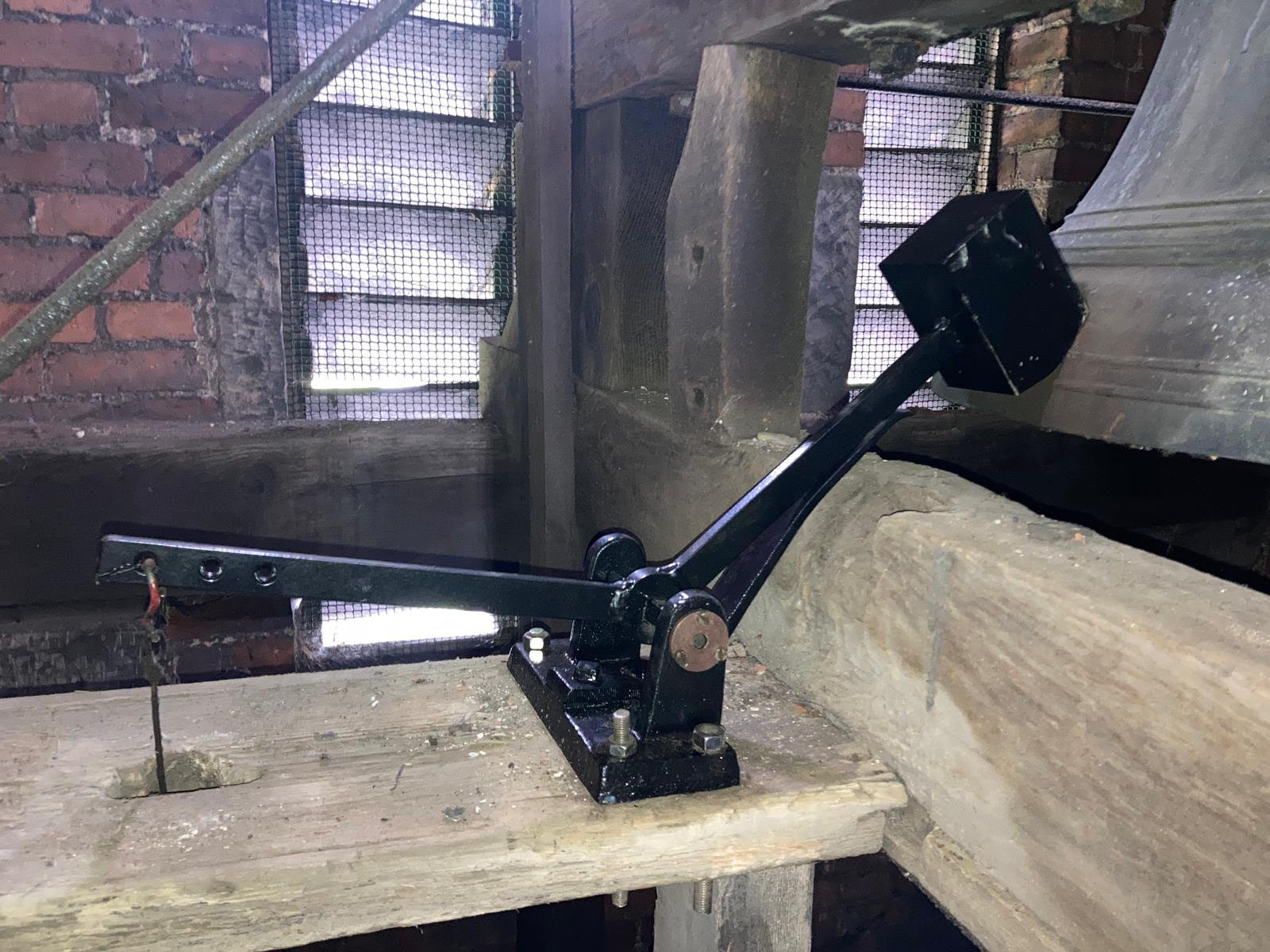 Shiny black metal bell hammer in situ at Holy Trinity Church, next to the bell